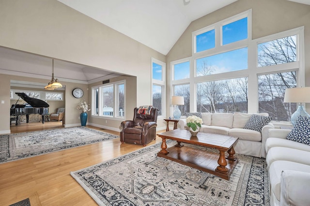 living area with plenty of natural light, baseboards, wood finished floors, and high vaulted ceiling