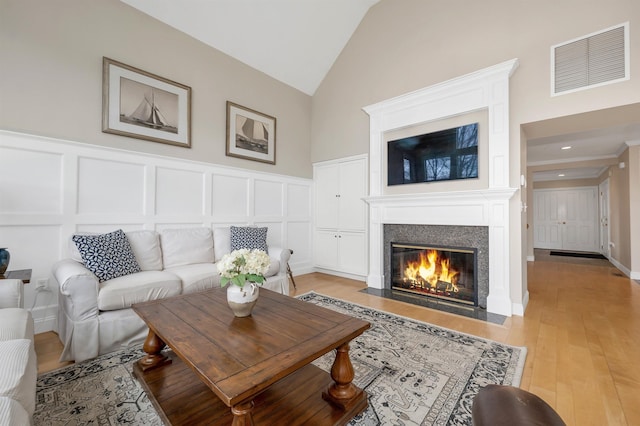 living area with a fireplace with flush hearth, visible vents, light wood-style floors, lofted ceiling, and a decorative wall