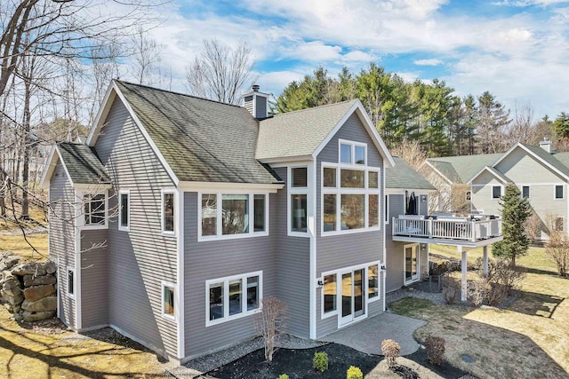 back of house with a chimney, a patio area, a deck, and a shingled roof