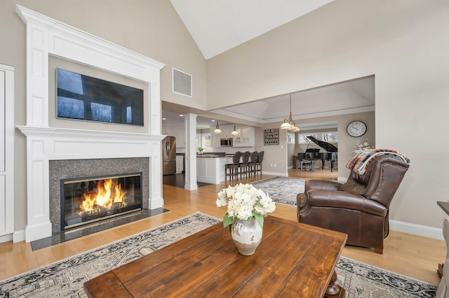 living room featuring a fireplace with flush hearth, vaulted ceiling, visible vents, and light wood-style floors