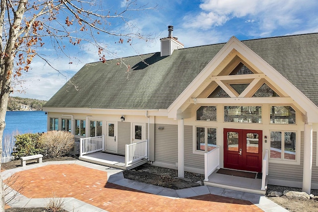 back of house featuring a chimney, a water view, a shingled roof, and covered porch