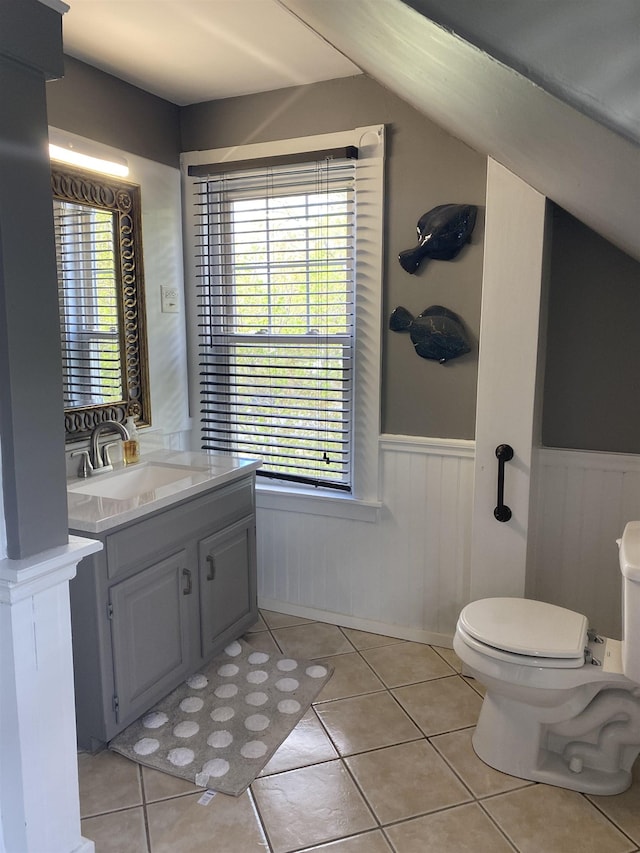 half bath featuring toilet, a wainscoted wall, tile patterned floors, and a wealth of natural light