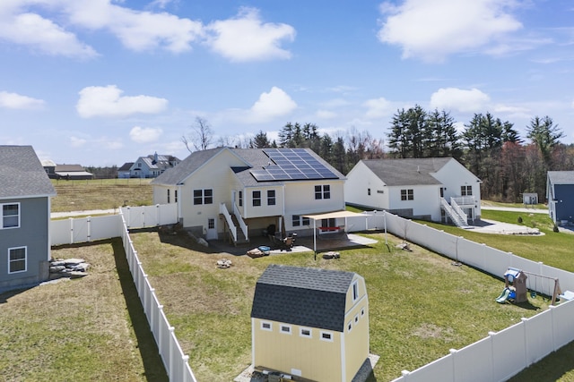 rear view of house with roof mounted solar panels, a fenced backyard, a storage shed, an outbuilding, and roof with shingles