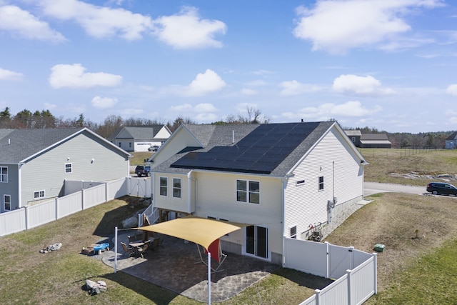 rear view of house featuring a gate, a shingled roof, a fenced backyard, solar panels, and a patio