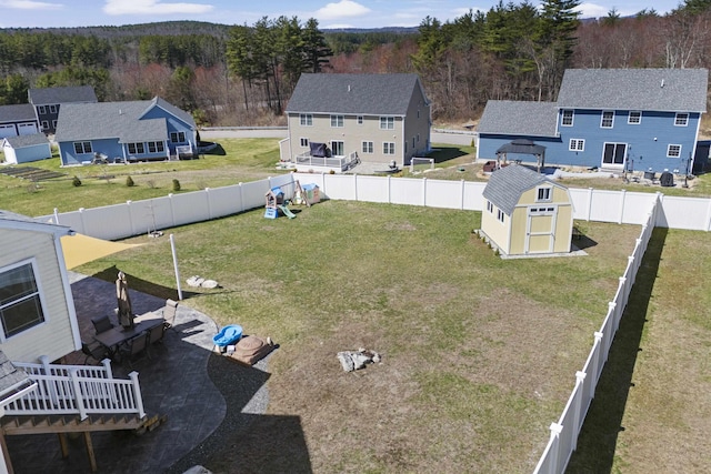 view of yard featuring a storage shed, a fenced backyard, a deck, an outdoor structure, and a forest view