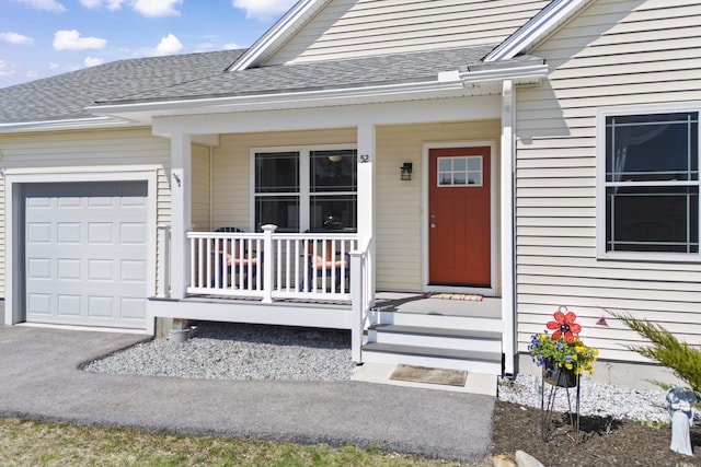 view of exterior entry with an attached garage, roof with shingles, and covered porch