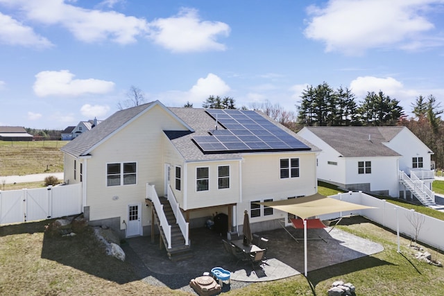 rear view of house with a gate, solar panels, a fenced backyard, and stairs