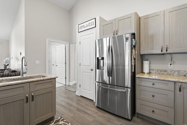 kitchen featuring light stone counters, wood finished floors, gray cabinets, a sink, and stainless steel fridge