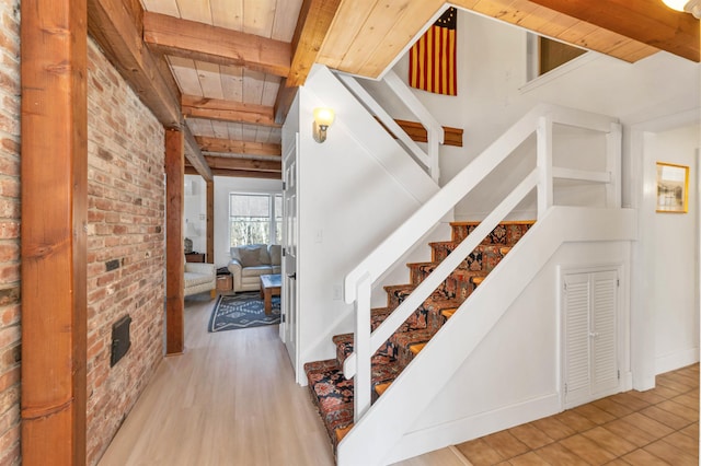 stairway featuring baseboards, beamed ceiling, brick wall, wood finished floors, and wood ceiling