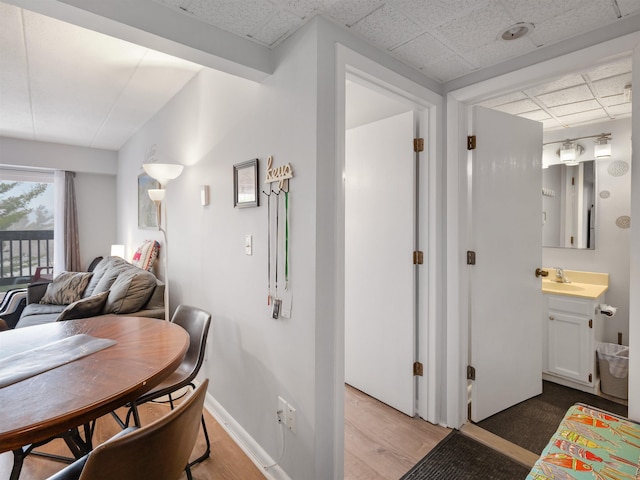dining room featuring baseboards, light wood-style floors, and a drop ceiling