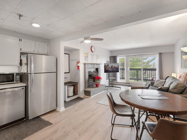 dining area with a fireplace, light wood finished floors, and ceiling fan