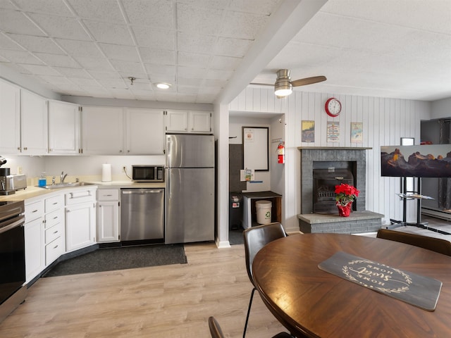 kitchen with stainless steel appliances, a sink, white cabinetry, light wood-style floors, and ceiling fan