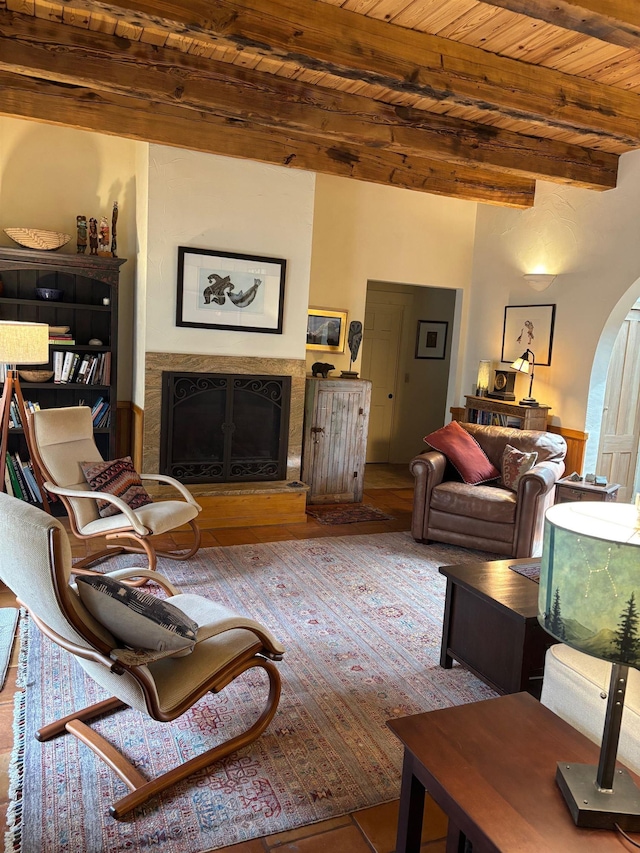 living area featuring a fireplace with raised hearth, wood finished floors, arched walkways, beam ceiling, and wood ceiling