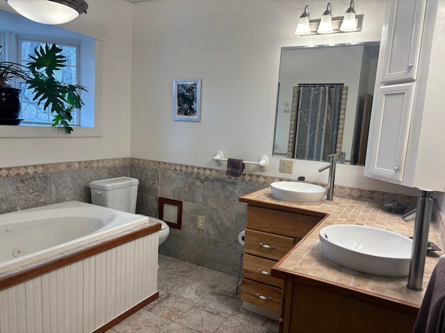 bathroom featuring tile walls, a wainscoted wall, a whirlpool tub, and a sink