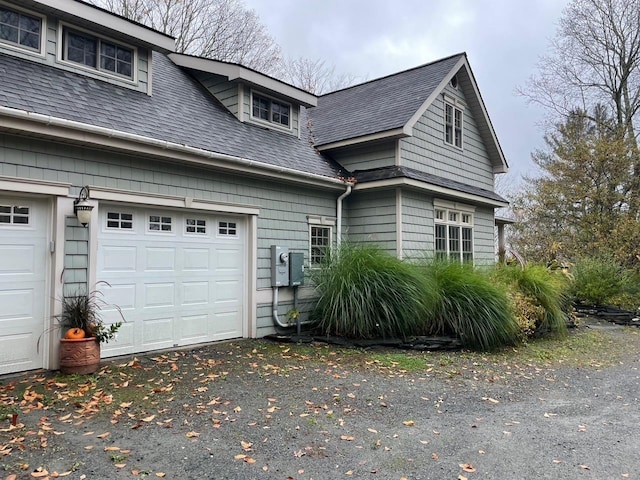 view of side of property with a shingled roof, driveway, and a garage