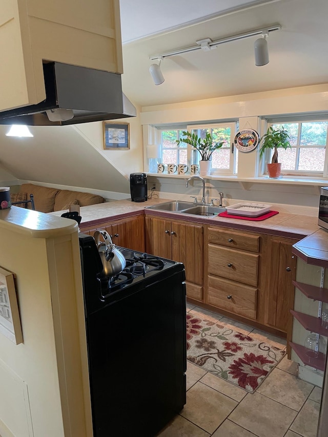 kitchen with track lighting, brown cabinetry, gas stove, and a sink