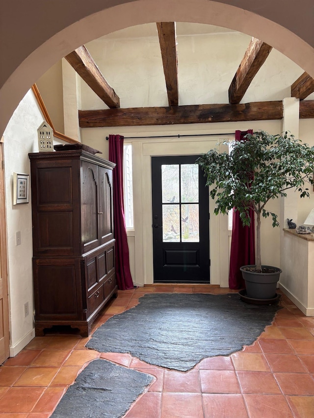 foyer with beam ceiling, baseboards, arched walkways, and light tile patterned floors