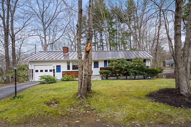 ranch-style home with a chimney, aphalt driveway, metal roof, a garage, and a standing seam roof