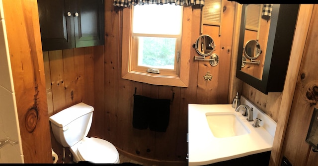 half bathroom featuring wooden walls, vanity, and toilet