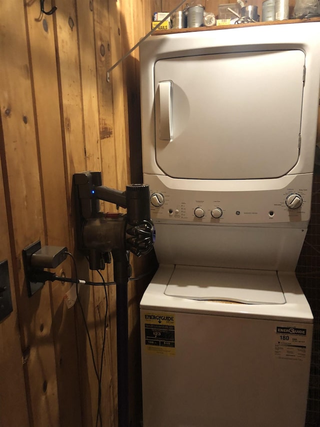 laundry room with wood walls, stacked washing maching and dryer, and laundry area