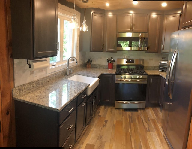 kitchen featuring light stone counters, appliances with stainless steel finishes, a sink, and light wood-style flooring