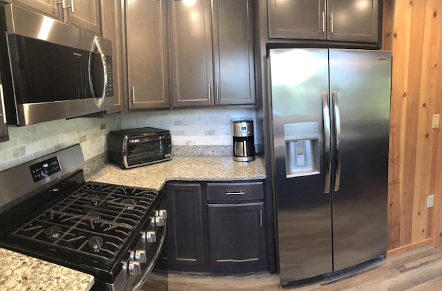 kitchen featuring backsplash, light stone countertops, stainless steel appliances, and light wood-style flooring
