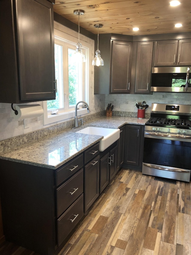 kitchen featuring stainless steel appliances, light wood-style flooring, a sink, decorative backsplash, and light stone counters