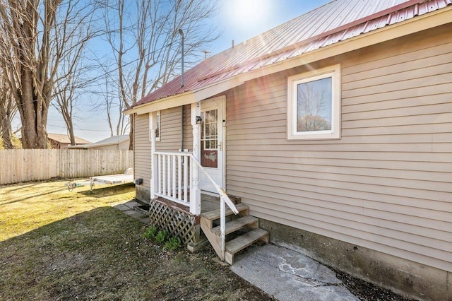 property entrance featuring a lawn, fence, and metal roof