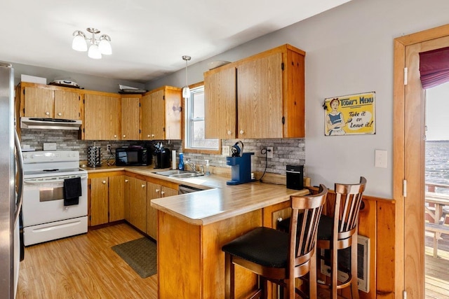 kitchen with a peninsula, ventilation hood, white electric range oven, a sink, and black microwave
