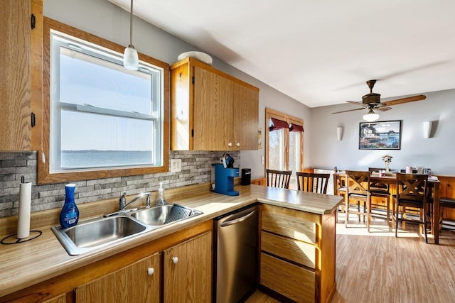 kitchen with a peninsula, stainless steel dishwasher, a sink, and light countertops