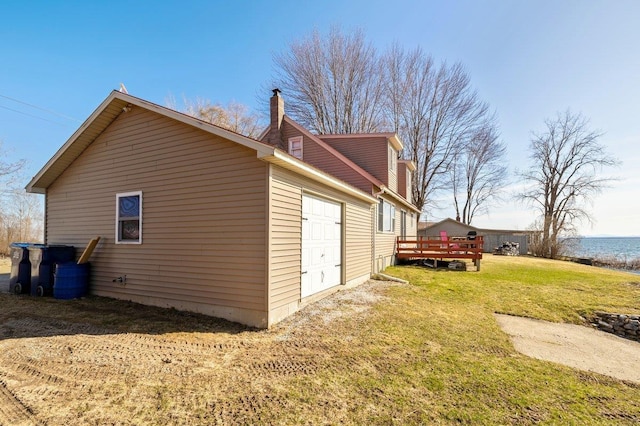 view of side of property featuring an attached garage, a lawn, a chimney, and a deck