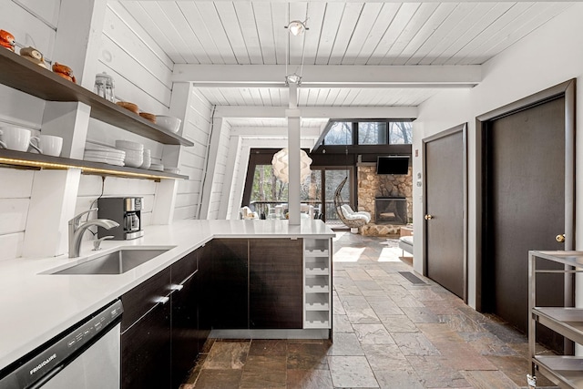 kitchen featuring light countertops, a sink, open shelves, dishwasher, and a fireplace