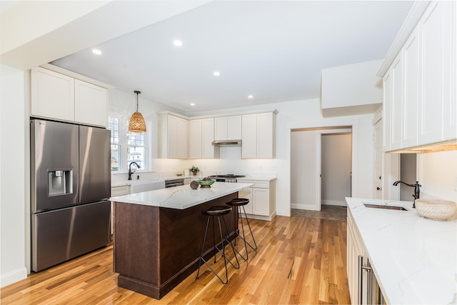kitchen with light stone counters, light wood-style floors, a sink, and stainless steel fridge with ice dispenser