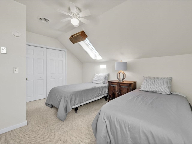 carpeted bedroom with vaulted ceiling with skylight, a closet, ceiling fan, baseboards, and visible vents