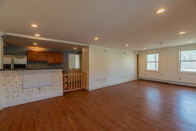 unfurnished living room featuring a baseboard heating unit, wood finished floors, and recessed lighting