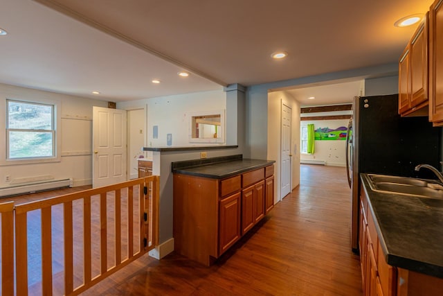 kitchen featuring brown cabinetry, dark countertops, a baseboard heating unit, and a sink
