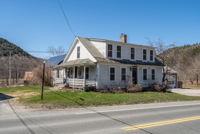 view of front facade featuring a chimney, a front lawn, and covered porch