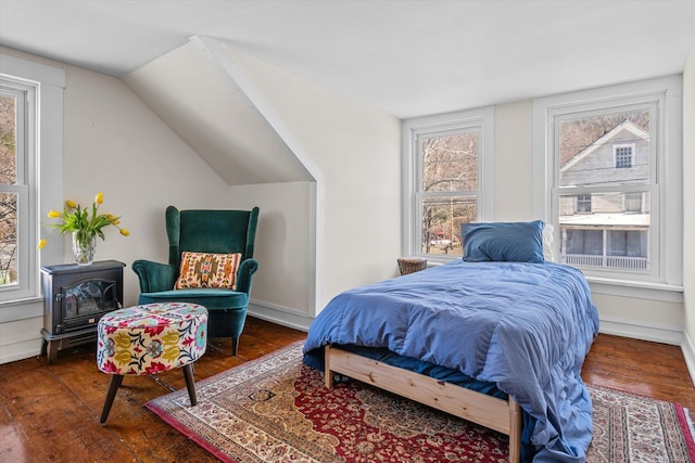 bedroom featuring wood-type flooring, vaulted ceiling, and a wood stove