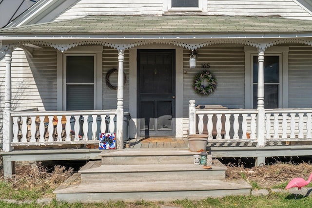 doorway to property featuring a porch and roof with shingles