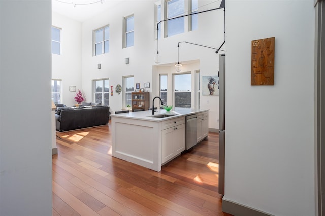 kitchen featuring white cabinets, stainless steel dishwasher, a sink, open floor plan, and wood-type flooring