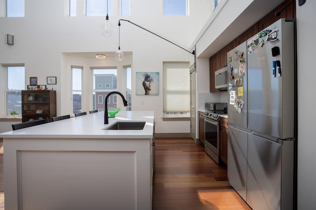 kitchen with an island with sink, light countertops, a sink, appliances with stainless steel finishes, and dark wood-style flooring