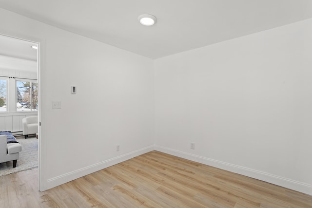 unfurnished room featuring light wood-type flooring, baseboards, and a baseboard radiator