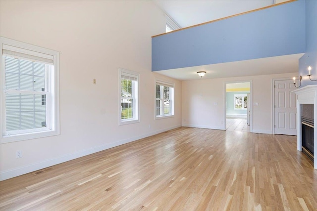 23 Hampton Mdws, Hampton, NH 03842 - unfurnished living room featuring baseboards, a towering ceiling, visible vents, and light wood-style floors