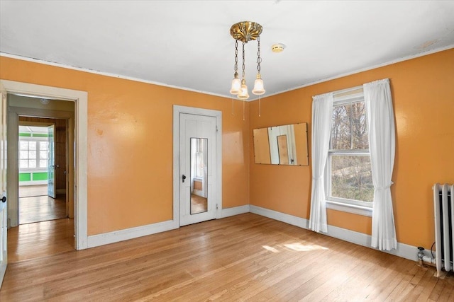 empty room featuring ornamental molding, baseboards, radiator heating unit, and light wood-style flooring