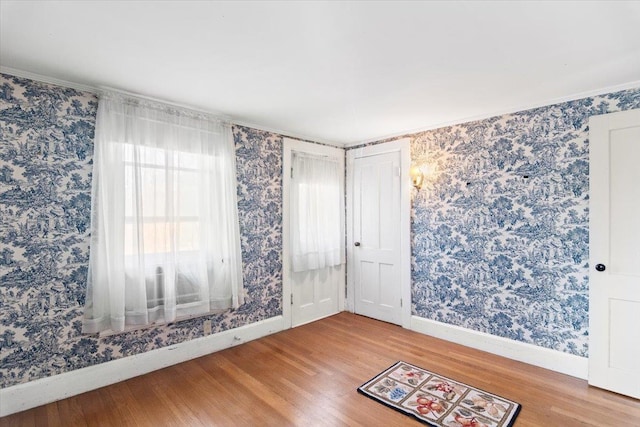 spare room featuring baseboards, wood finished floors, ornamental molding, and wallpapered walls