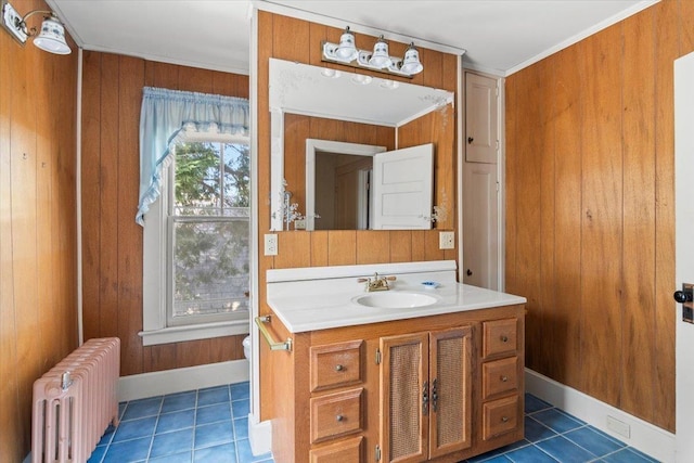 half bathroom featuring radiator, tile patterned flooring, crown molding, wooden walls, and vanity