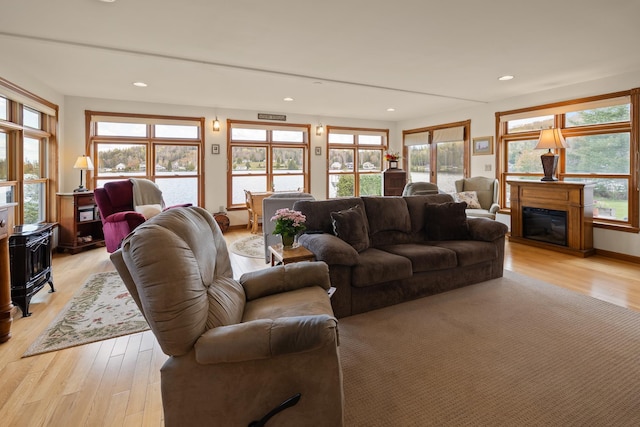 living room featuring recessed lighting, a glass covered fireplace, a water view, and light wood-type flooring