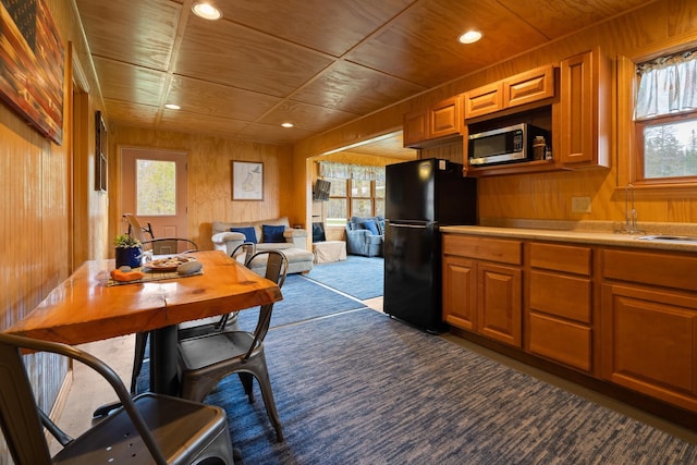 kitchen with stainless steel microwave, freestanding refrigerator, carpet floors, and wooden walls
