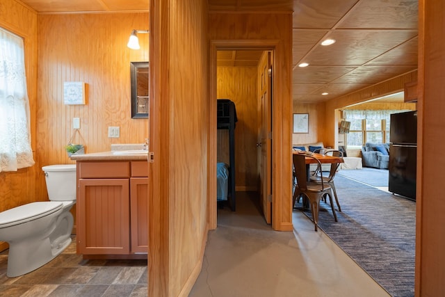half bathroom with wooden walls, vanity, recessed lighting, and toilet