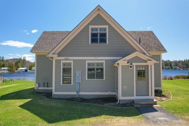 view of front of home with a shingled roof, a front lawn, and a water view